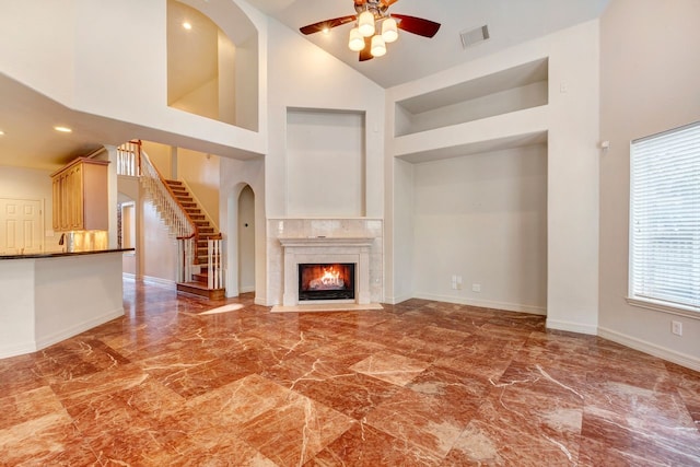 unfurnished living room with a high end fireplace, ceiling fan, and high vaulted ceiling