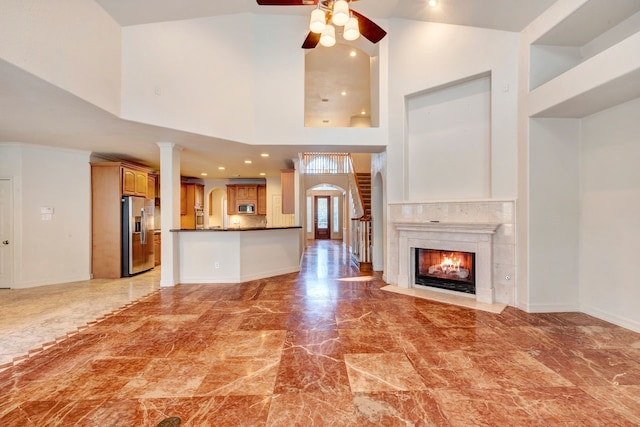 unfurnished living room with a premium fireplace, a towering ceiling, and ceiling fan