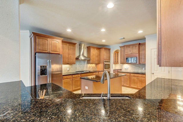 kitchen with dark stone counters, wall chimney range hood, sink, ornamental molding, and appliances with stainless steel finishes