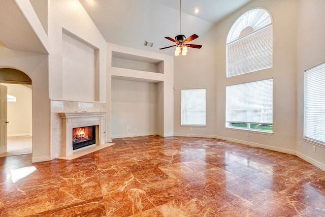 unfurnished living room with ceiling fan, built in features, a high end fireplace, and high vaulted ceiling