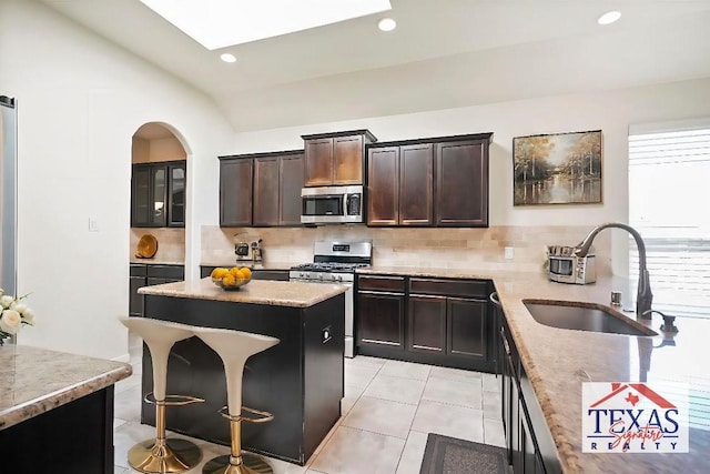 kitchen featuring lofted ceiling, backsplash, sink, appliances with stainless steel finishes, and a kitchen island