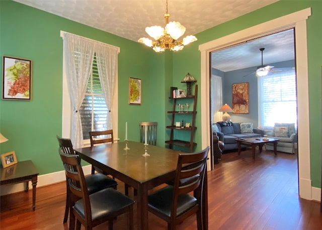 dining space with a textured ceiling, ceiling fan with notable chandelier, and dark wood-type flooring