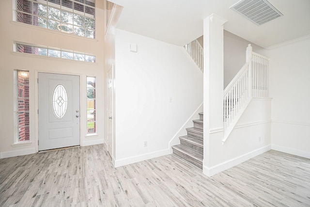 foyer entrance with ornamental molding, a high ceiling, and light hardwood / wood-style flooring