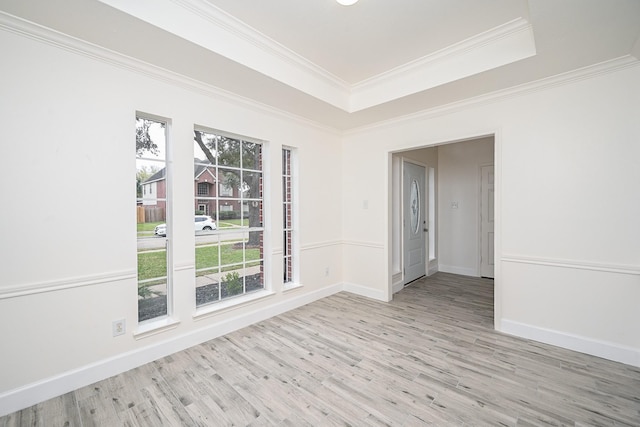 empty room featuring a raised ceiling, light hardwood / wood-style flooring, and ornamental molding