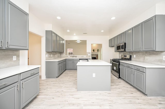 kitchen featuring gray cabinetry, sink, a center island, backsplash, and appliances with stainless steel finishes