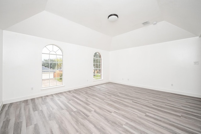 unfurnished room featuring lofted ceiling, a raised ceiling, and light wood-type flooring