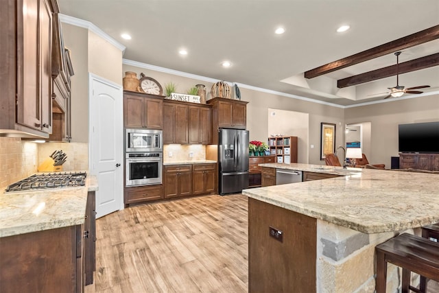 kitchen with a sink, stainless steel appliances, light wood-style floors, a kitchen bar, and backsplash