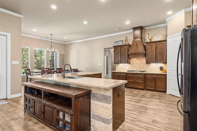 kitchen with light wood finished floors, freestanding refrigerator, a sink, custom range hood, and stainless steel gas stovetop