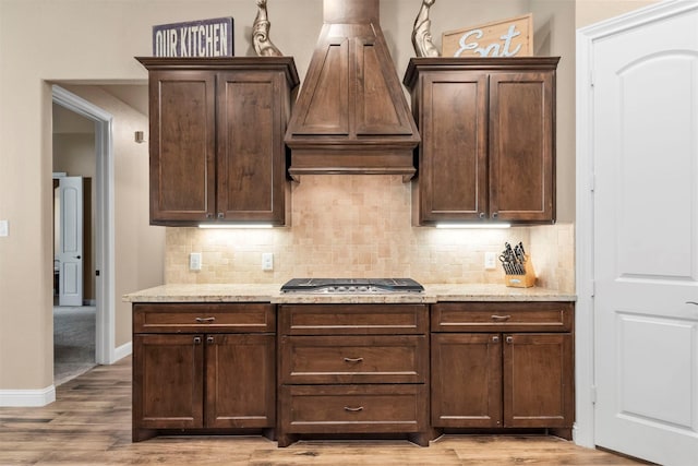 kitchen with decorative backsplash, custom range hood, light stone countertops, and stainless steel gas cooktop