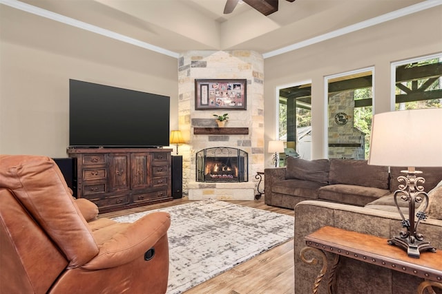 living area with a stone fireplace, crown molding, ceiling fan, and wood finished floors