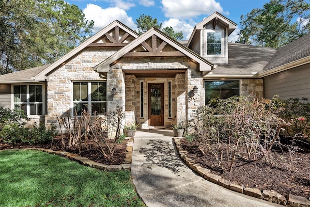 doorway to property featuring stone siding and roof with shingles