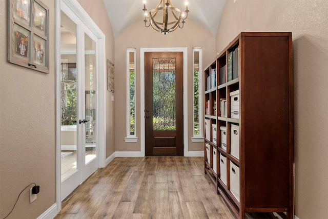 foyer with an inviting chandelier, lofted ceiling, wood finished floors, and baseboards