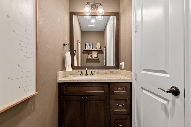 bathroom featuring visible vents, vanity, and a textured wall