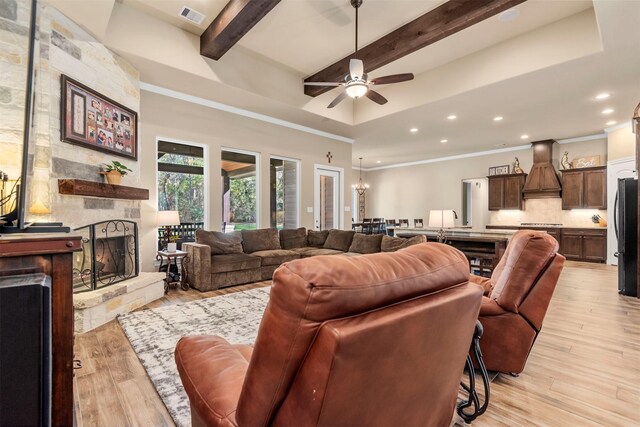 living room with a stone fireplace, light wood-style flooring, beamed ceiling, and visible vents