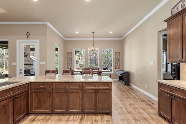 kitchen with crown molding, baseboards, decorative light fixtures, light stone counters, and light wood-style flooring