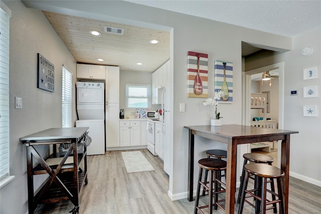 kitchen with light wood-type flooring, white cabinetry, stacked washer / dryer, and ceiling fan