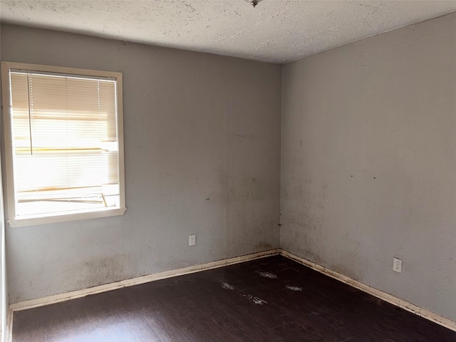 spare room featuring a textured ceiling and dark hardwood / wood-style flooring