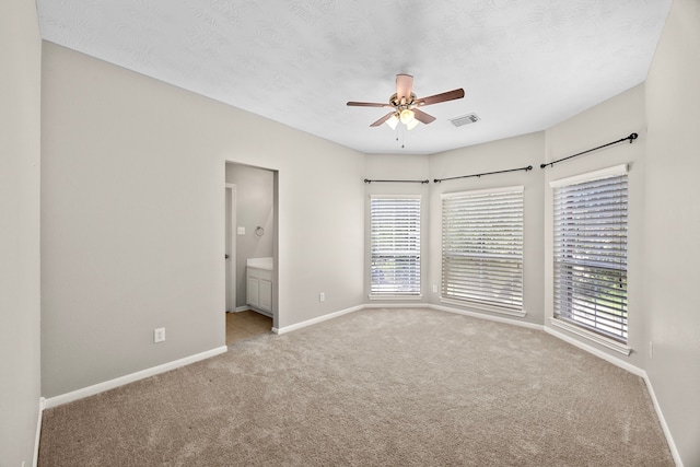 unfurnished bedroom featuring light carpet, a textured ceiling, ensuite bathroom, and ceiling fan