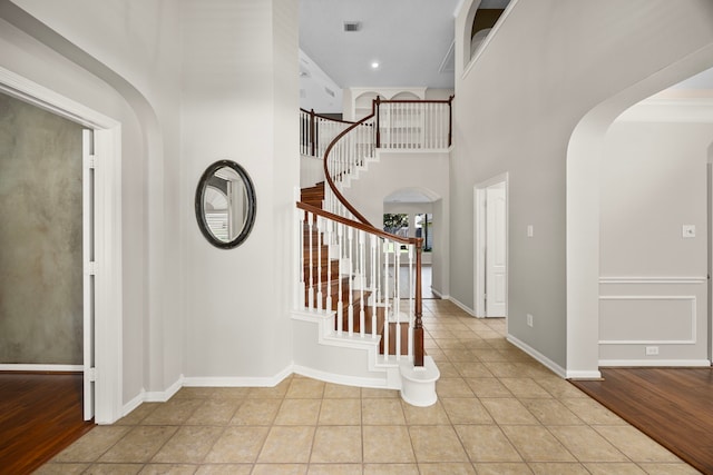 entryway with light hardwood / wood-style floors, a towering ceiling, and crown molding