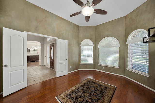 unfurnished room with hardwood / wood-style floors, a towering ceiling, and ceiling fan with notable chandelier