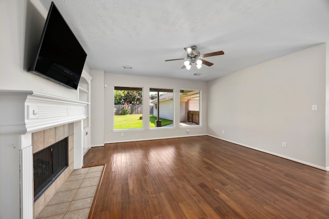 unfurnished living room featuring a tile fireplace, ceiling fan, light hardwood / wood-style flooring, and a textured ceiling