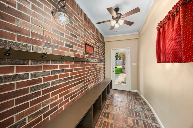 entryway featuring ceiling fan, brick wall, and ornamental molding