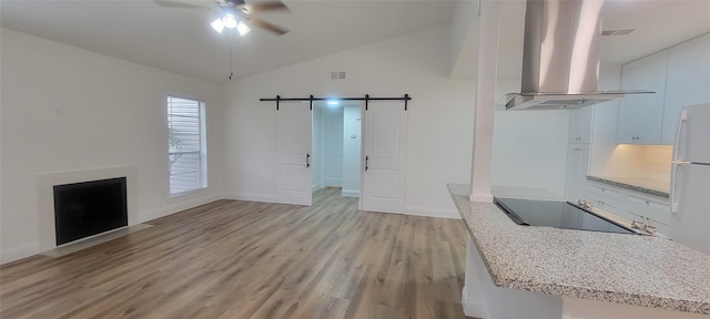 unfurnished living room featuring lofted ceiling, a barn door, ceiling fan, and light hardwood / wood-style floors