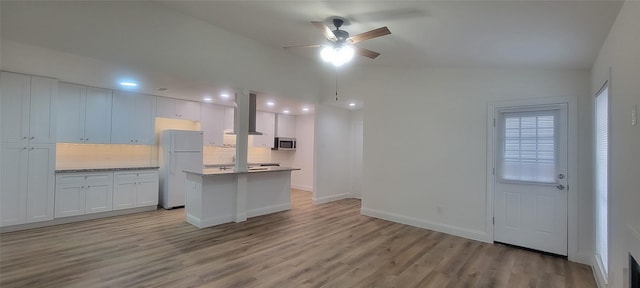 kitchen featuring vaulted ceiling, backsplash, wall chimney range hood, white cabinets, and white refrigerator