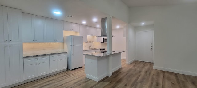 kitchen with white cabinetry, island exhaust hood, backsplash, light stone countertops, and white refrigerator