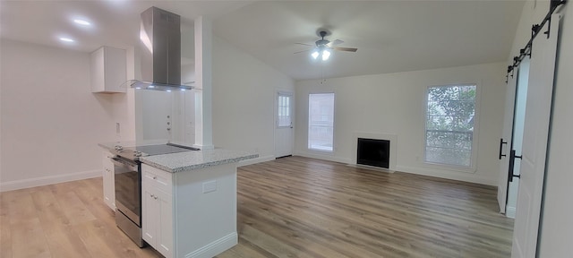 kitchen with ceiling fan, a barn door, range hood, stainless steel electric stove, and white cabinets