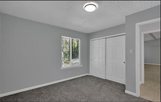 unfurnished bedroom featuring a textured ceiling, dark carpet, and a closet