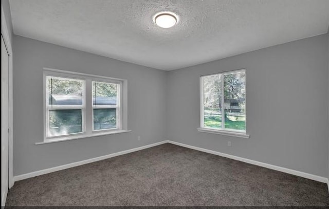 spare room featuring dark colored carpet and a textured ceiling