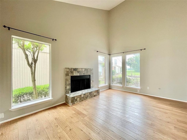 unfurnished living room featuring a fireplace, a towering ceiling, and light wood-type flooring