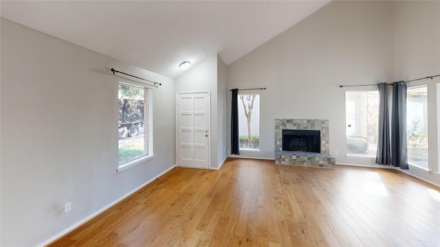 unfurnished living room with a fireplace, light hardwood / wood-style flooring, high vaulted ceiling, and a healthy amount of sunlight