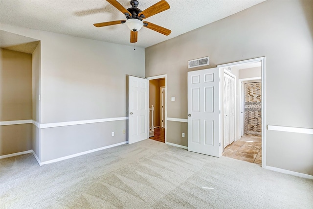 unfurnished bedroom with a textured ceiling, ceiling fan, light carpet, and ensuite bath