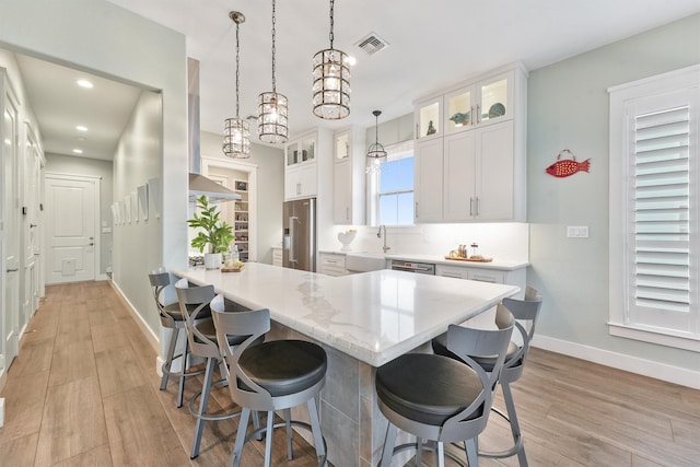 kitchen featuring visible vents, light wood finished floors, stainless steel appliances, white cabinets, and a kitchen breakfast bar