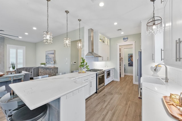 kitchen featuring stainless steel range, a sink, a peninsula, wall chimney exhaust hood, and white cabinets