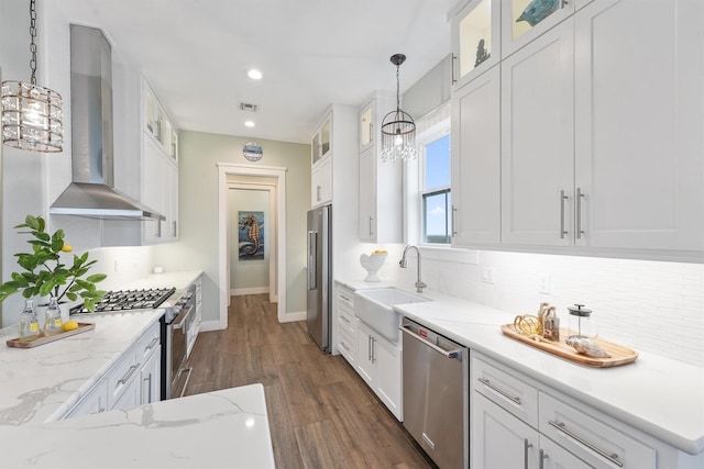 kitchen with sink, wall chimney exhaust hood, pendant lighting, high quality appliances, and white cabinets