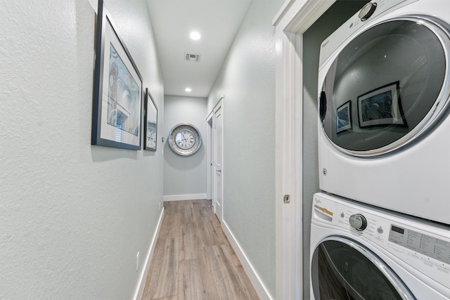 washroom with light wood-type flooring, visible vents, stacked washer / drying machine, baseboards, and laundry area