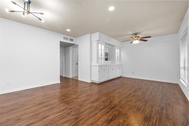 unfurnished living room featuring ceiling fan with notable chandelier, dark wood-type flooring, a textured ceiling, and ornamental molding