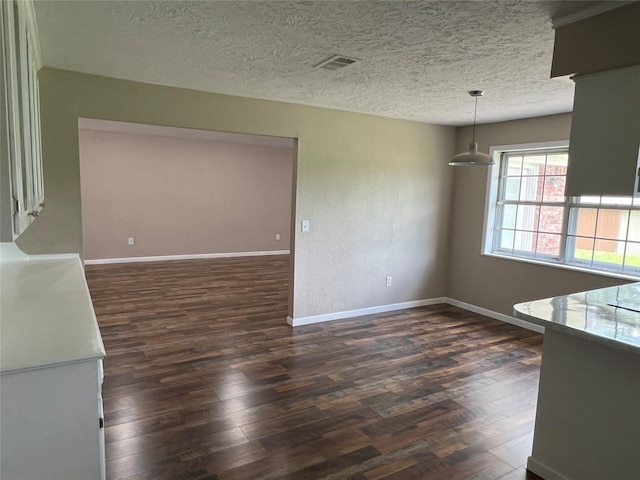 unfurnished dining area featuring a textured ceiling and dark wood-type flooring