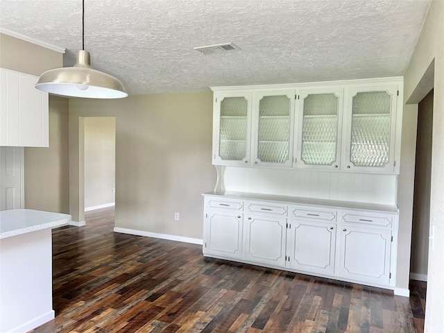 kitchen with dark wood-type flooring, white cabinets, hanging light fixtures, and a textured ceiling