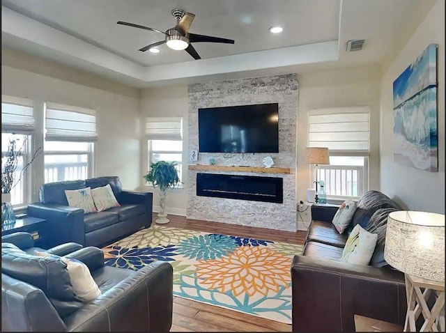 living room featuring a tray ceiling, ceiling fan, a fireplace, and wood-type flooring