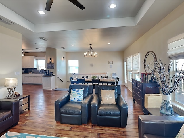 living room with a raised ceiling, wood-type flooring, and ceiling fan with notable chandelier