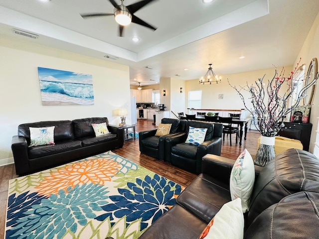 living room with hardwood / wood-style floors, ceiling fan with notable chandelier, and a raised ceiling