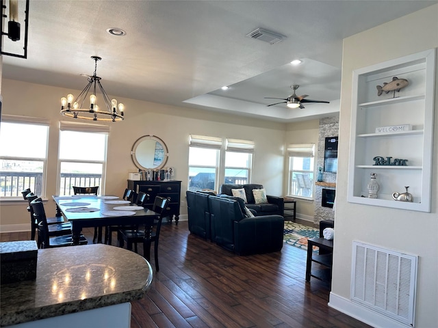 dining area with dark hardwood / wood-style floors, a fireplace, ceiling fan with notable chandelier, and built in shelves