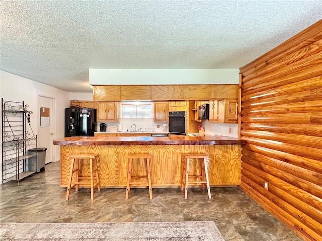 kitchen with kitchen peninsula, a kitchen bar, rustic walls, a textured ceiling, and black appliances