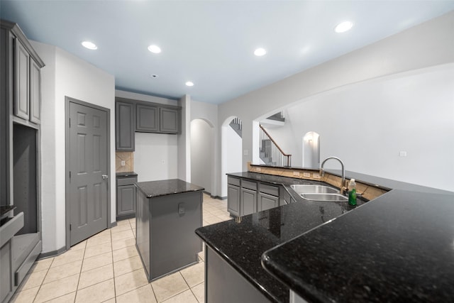 kitchen with gray cabinetry, a kitchen island, dark stone countertops, and sink