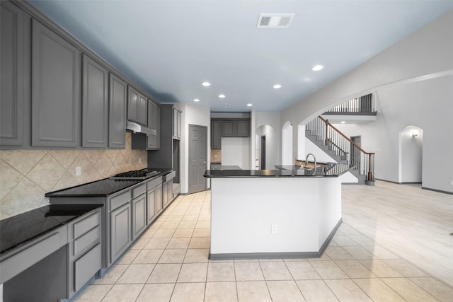 kitchen featuring gray cabinetry, decorative backsplash, an island with sink, and light tile patterned floors