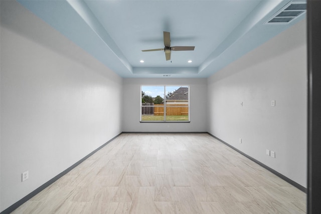 empty room with ceiling fan and a raised ceiling